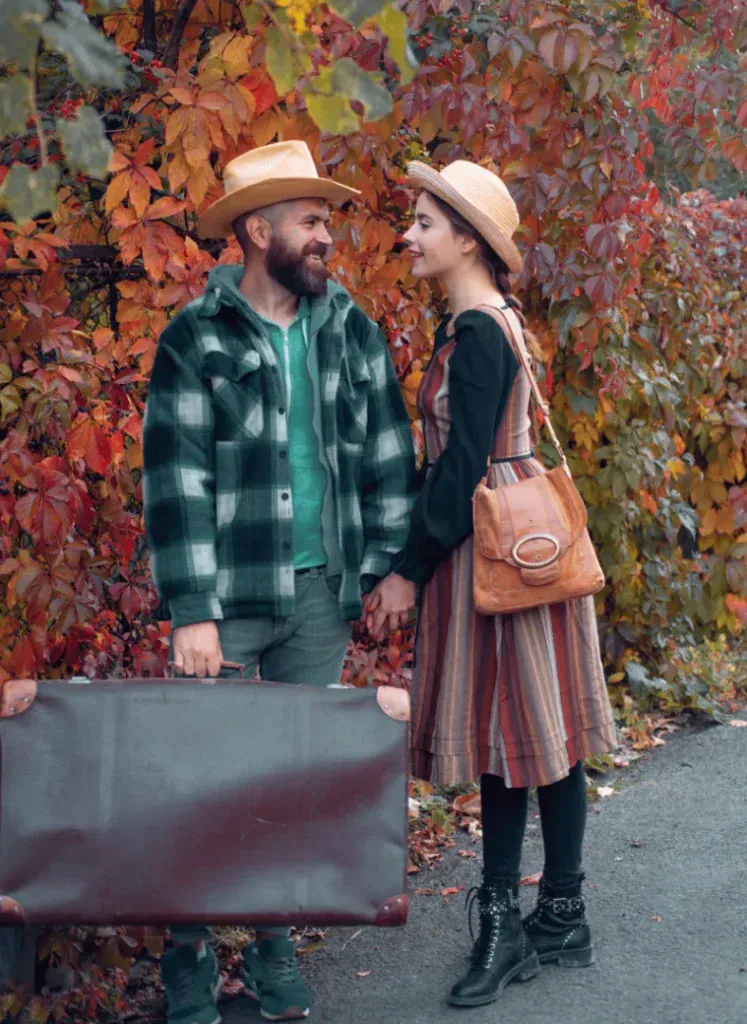 A couple holding hands with a suitcase, in front of red and gold autumn leaves